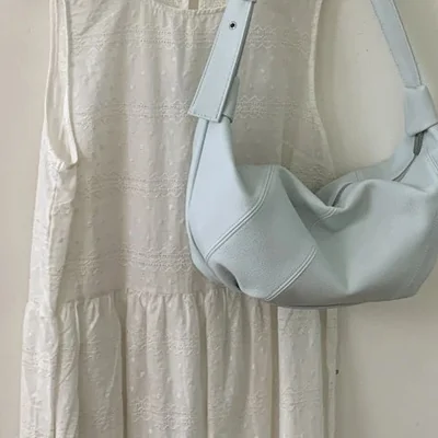 White eyelet sundress on a hanger with a pale blue slouchy crossbody bag hanging beside it
